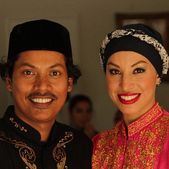 Alfira and Bang pose smiling for the camera in colourful traditional Indonesian dance clothes, photo is head and shoulder shot